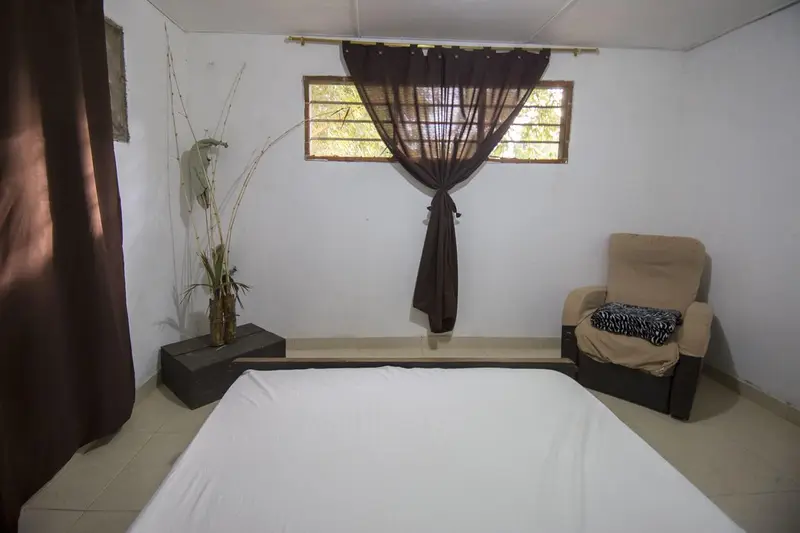 A bedroom corner with a curtain over the window, a plant and an upholstered armchair