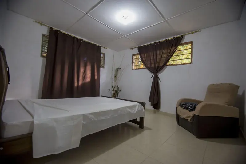 A tidy bedroom with a made bed, white walls and a dark brown curtain hanging in the doorway