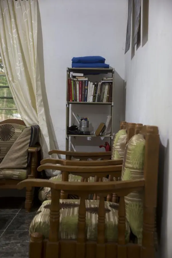 A bookshelf with folded towels and books next to wooden armchairs and a curtained window