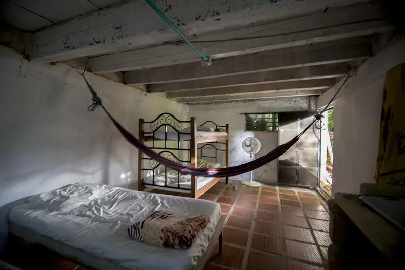 A room with a bunk bed, a single bed and a hammock under a metal roof