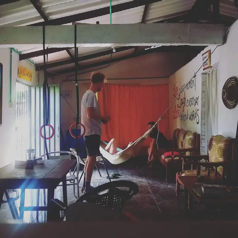 The open common room with a metal roof, gymnastic rings, a hammock, wooden chairs and a red curtain