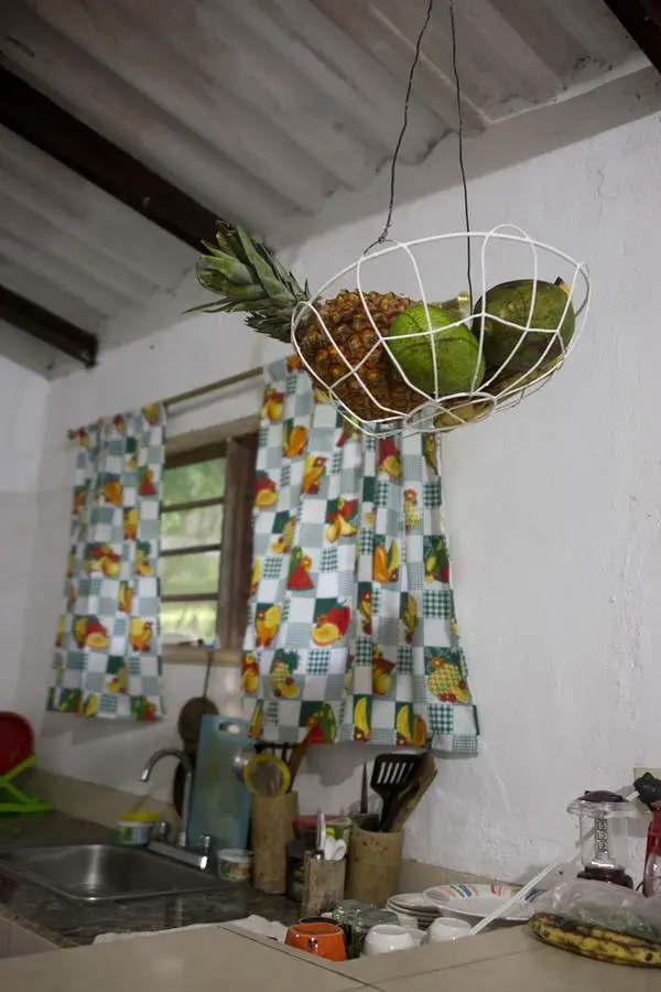 A hanging wire basket with a pineapple and fruit over the kitchen sink, patchwork curtain behind