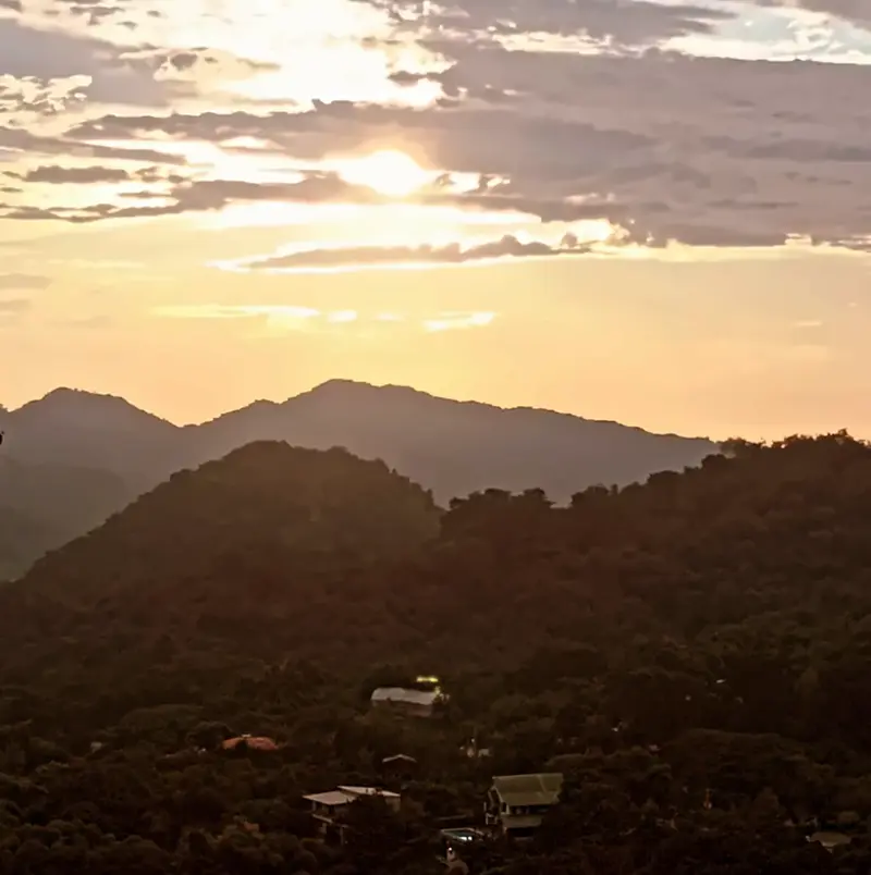 Golden sunset behind forested hills above Minca, with a few roofs among the trees