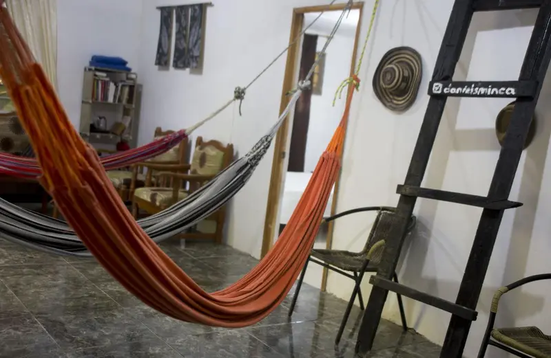 An orange hammock beside a black ladder in the common room, with a shelf and a decorative plate on the wall