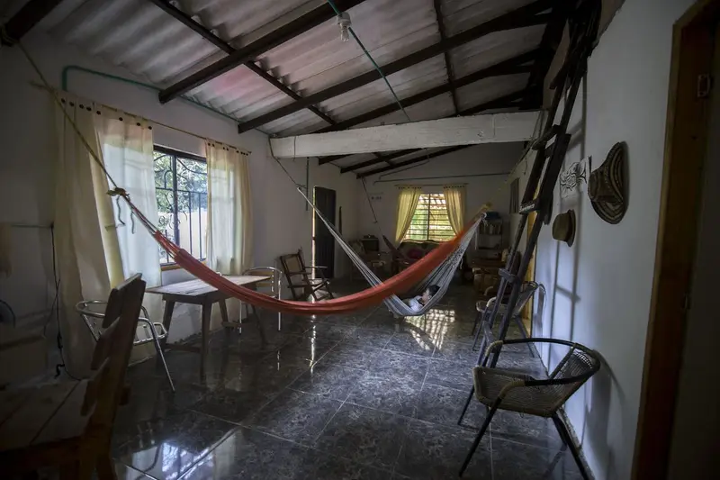 A red hammock by a window with curtains, a ladder leaning on the wall