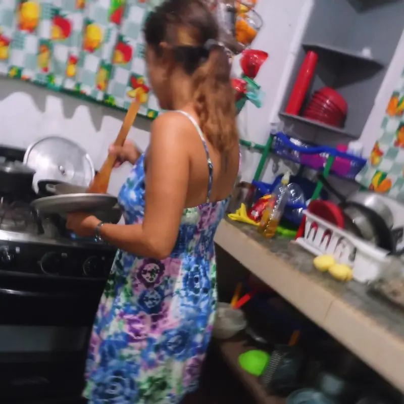 A guest in a flowered dress cooking at the stove of a colourful kitchen with red pots and patterned tiles