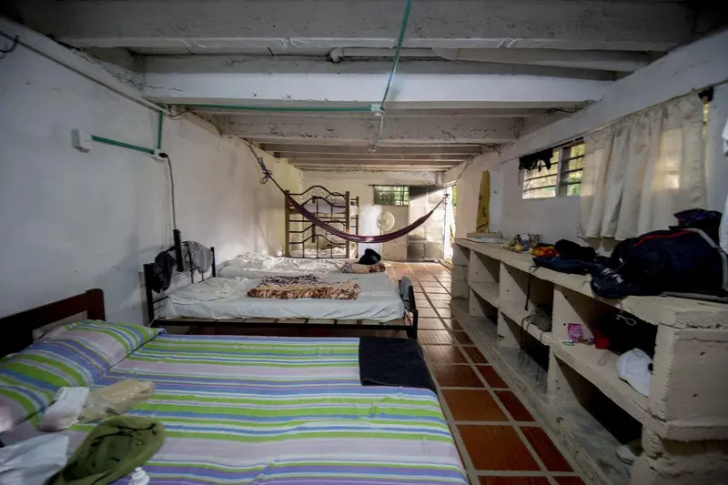 Two beds with striped sheets along a long room with open shelves and backpacks
