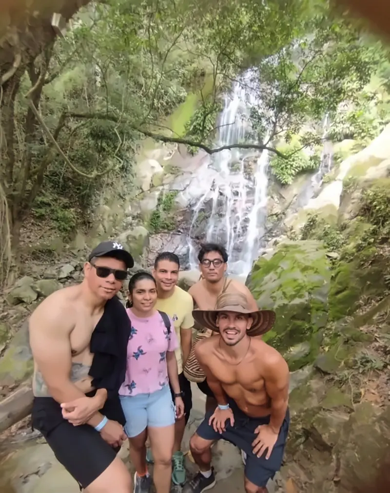 A group of five smiling hikers posing in front of a tall waterfall at Cascadas de Marinka