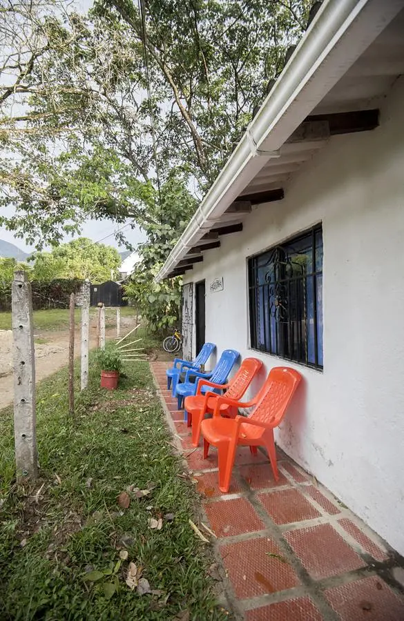 Orange and blue plastic chairs lined up on a tiled porch along the white wall of the house