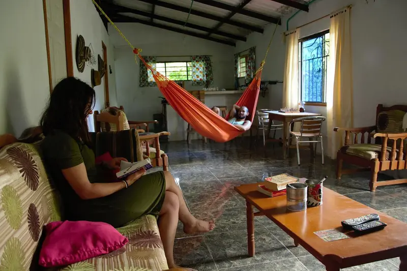 A guest reading on a cushioned bench in the common room, a hammock and chairs behind her