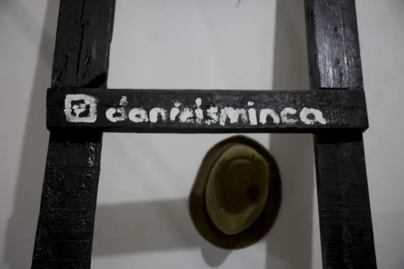A wooden frame with @danielsminca painted on it and a straw hat hanging on the wall below