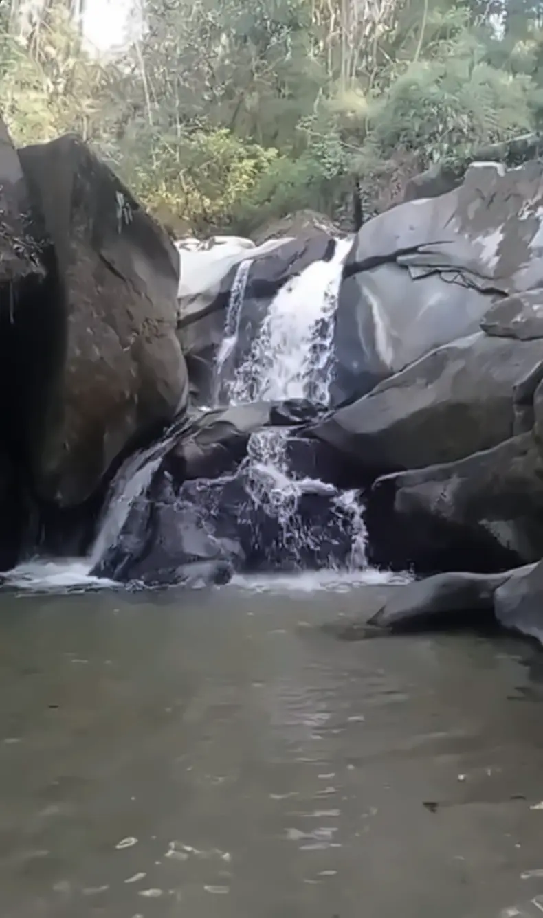 A small waterfall pouring between dark rocks into a calm natural pool
